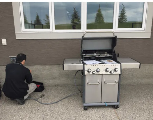A technician connecting a gas line to an outdoor barbecue grill on a patio