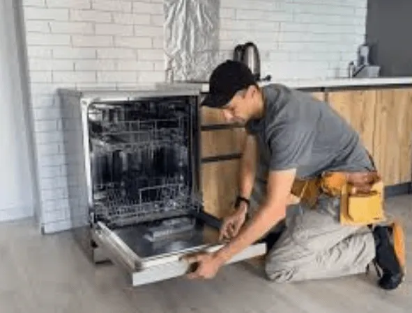 A technician sliding a new dishwasher into place under a kitchen counter