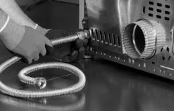 A technician connecting a flexible gas line to the back of a dryer