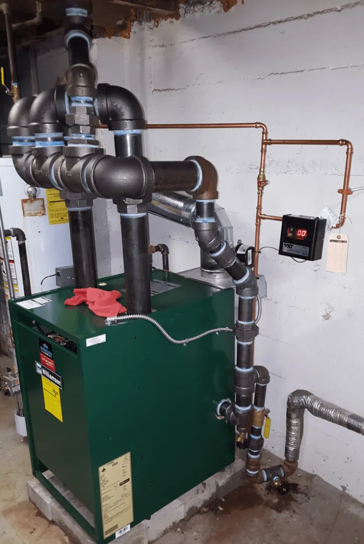 A new green gas steam boiler installed in a basement with fresh black iron piping
