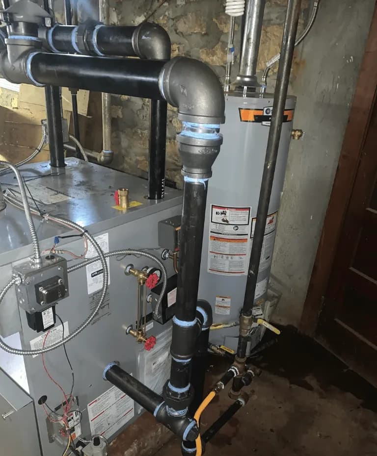 A Mr. Tankless technician working on a steam boiler and its piping in a basement